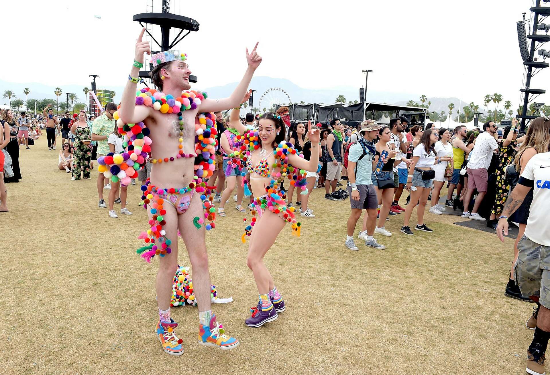 Two Coachella attendees wearing creative pom-pom costumes, dancing joyfully in front of a crowd at the festival