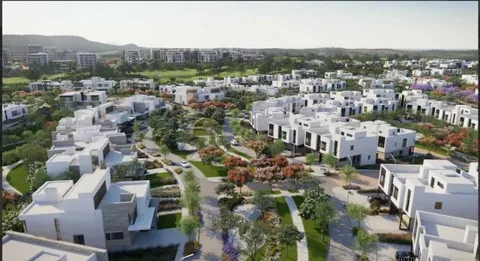"Aerial view of a modern residential real estate community with white contemporary houses, landscaped gardens, and winding pathways under clear sky."