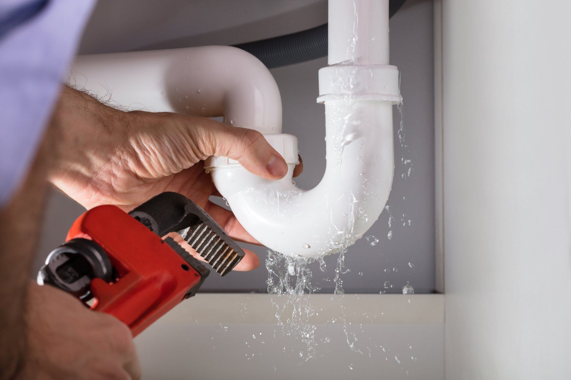 Plumber performing drain and pipe repairs under a sink